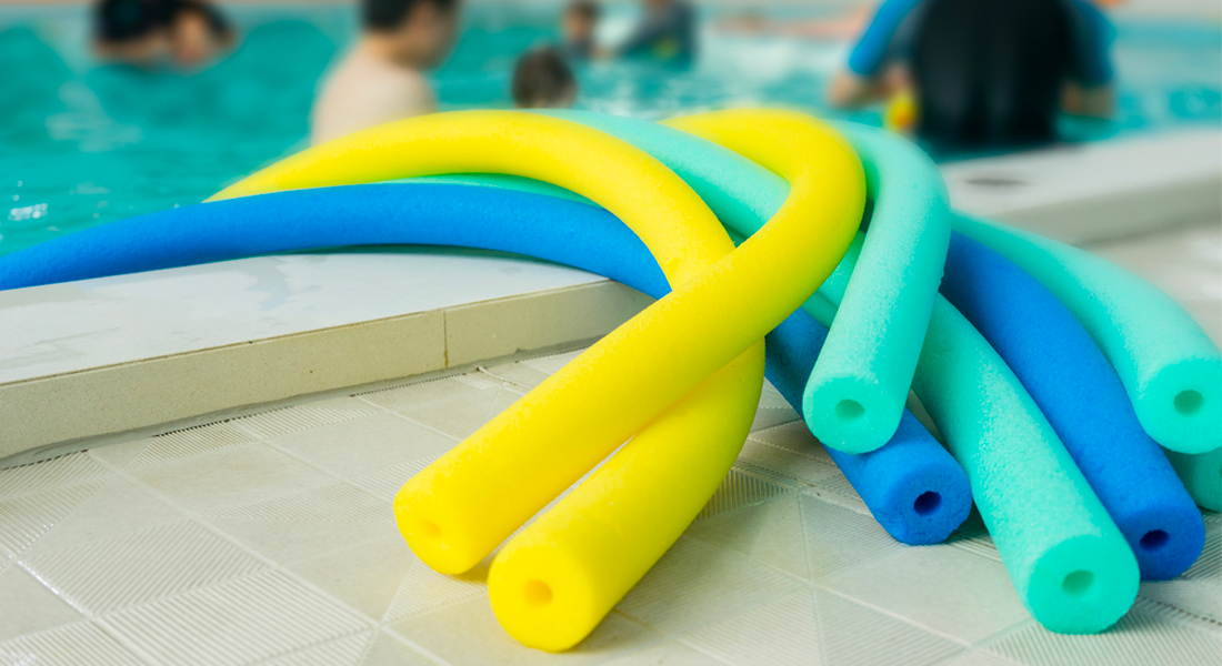 Žluté, zelené a modré bazénové nudle na kraji bazénu